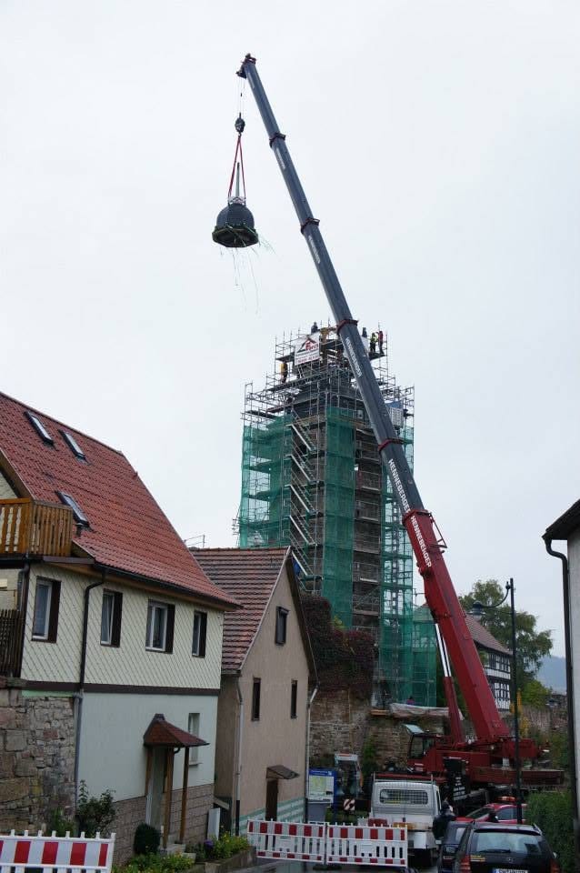 Ein Autokran hebt die Turmhaube zum eingerüsteten Kirchturm